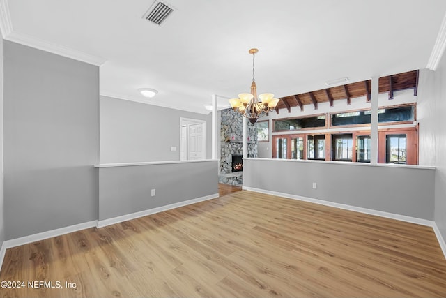 spare room with light hardwood / wood-style floors, a stone fireplace, ornamental molding, and a chandelier