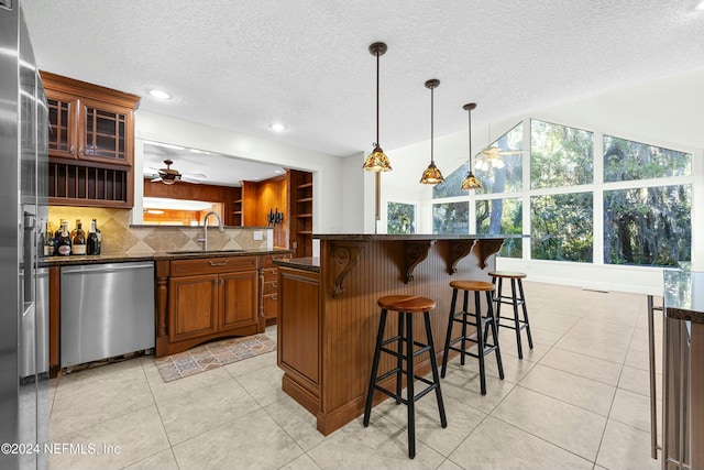 kitchen with decorative backsplash, a kitchen breakfast bar, sink, dishwasher, and hanging light fixtures