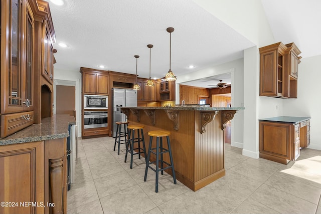 kitchen featuring ceiling fan, stainless steel appliances, pendant lighting, a kitchen bar, and light tile patterned flooring