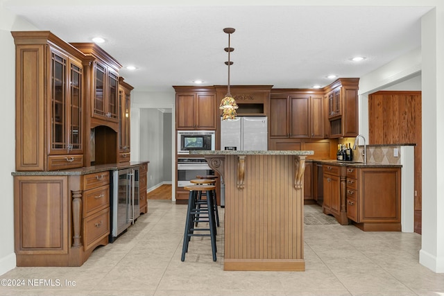 kitchen featuring white refrigerator with ice dispenser, hanging light fixtures, wine cooler, dark stone countertops, and a breakfast bar area