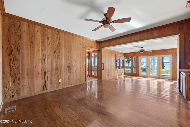 unfurnished living room featuring hardwood / wood-style flooring, wood walls, and french doors