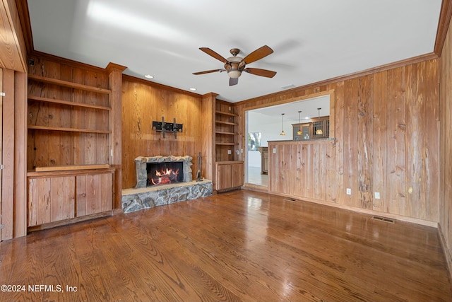 unfurnished living room featuring wood walls, a fireplace, wood-type flooring, and ornamental molding