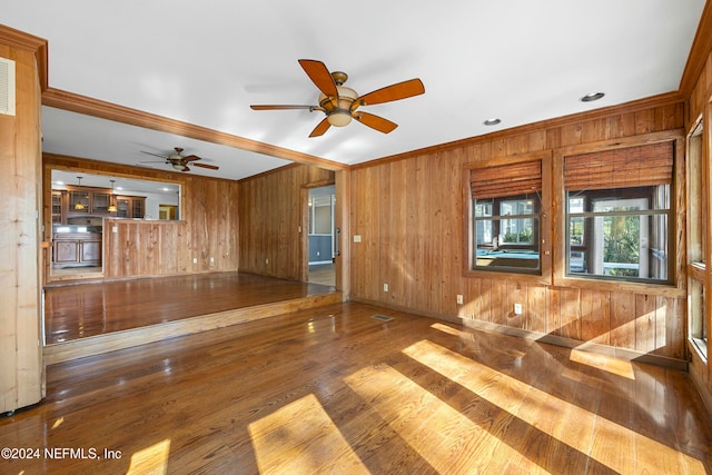 unfurnished living room with hardwood / wood-style flooring, ceiling fan, wood walls, and crown molding