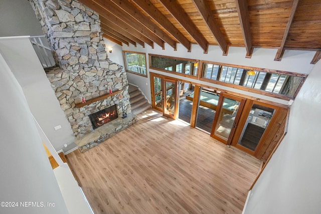 living room featuring beam ceiling, a high ceiling, a stone fireplace, wood-type flooring, and wood ceiling