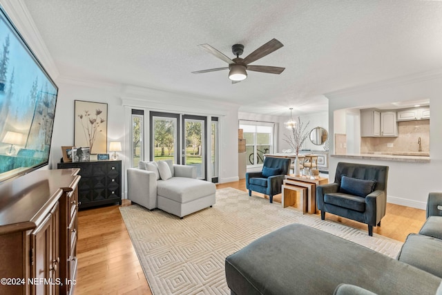 living room with a textured ceiling, ceiling fan with notable chandelier, crown molding, and light hardwood / wood-style flooring