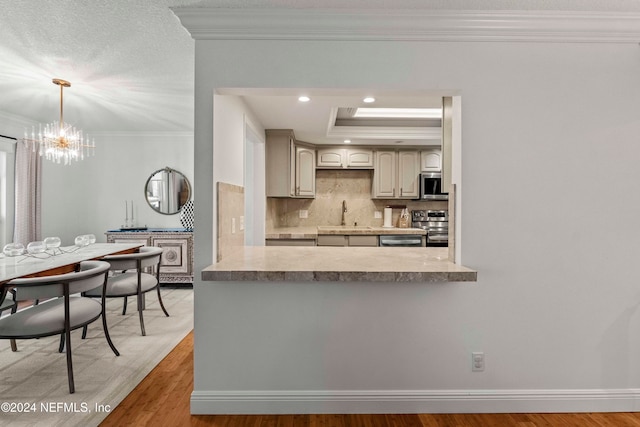 kitchen featuring light wood-type flooring, ornamental molding, stainless steel appliances, sink, and a chandelier