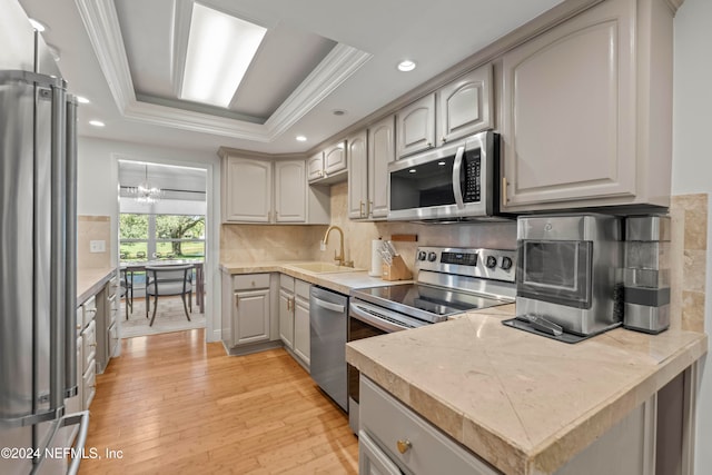 kitchen with a notable chandelier, light hardwood / wood-style floors, a tray ceiling, gray cabinets, and appliances with stainless steel finishes