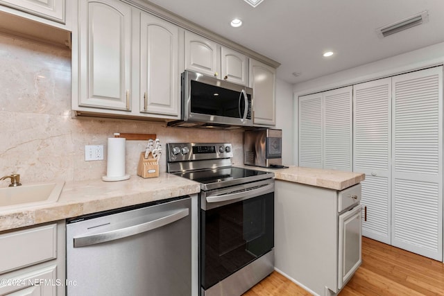 kitchen with decorative backsplash, appliances with stainless steel finishes, light wood-type flooring, and sink