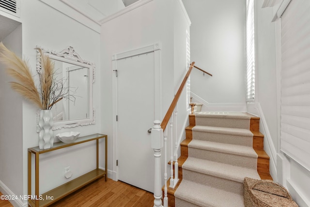 stairs featuring wood-type flooring and ornamental molding