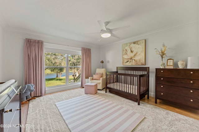 bedroom featuring ceiling fan, crown molding, a nursery area, and light hardwood / wood-style floors