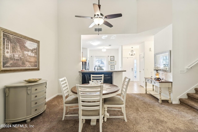 carpeted dining space featuring ceiling fan with notable chandelier, a towering ceiling, and sink