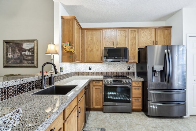 kitchen with light stone countertops, appliances with stainless steel finishes, a textured ceiling, sink, and light tile patterned floors