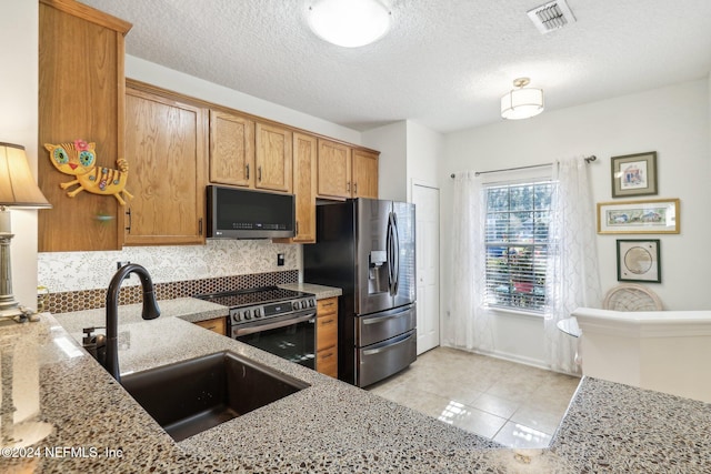 kitchen with sink, light stone countertops, a textured ceiling, appliances with stainless steel finishes, and light tile patterned flooring