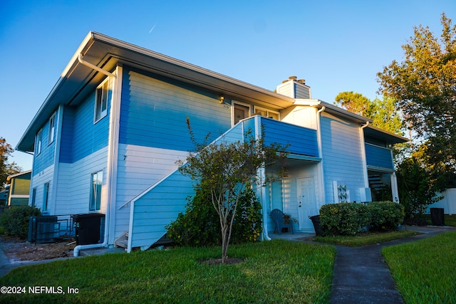 view of front of property with central AC, a balcony, and a front yard