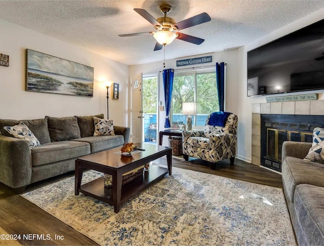 living room featuring a tile fireplace, ceiling fan, dark wood-type flooring, and a textured ceiling