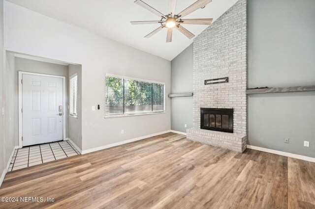 unfurnished living room featuring a brick fireplace, ceiling fan, high vaulted ceiling, and light wood-type flooring