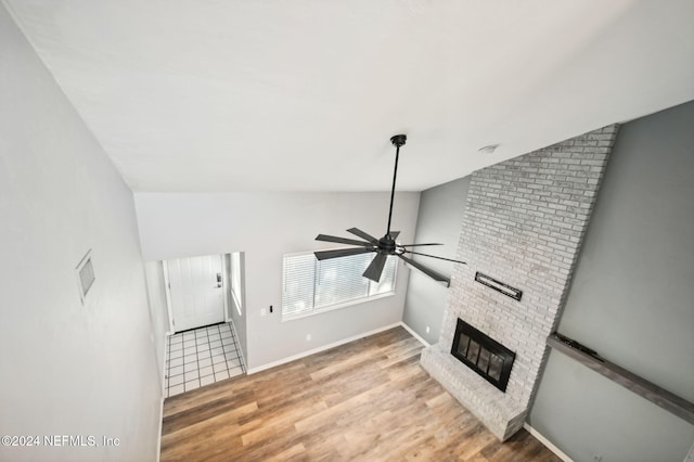 living room featuring ceiling fan, wood-type flooring, lofted ceiling, and a brick fireplace