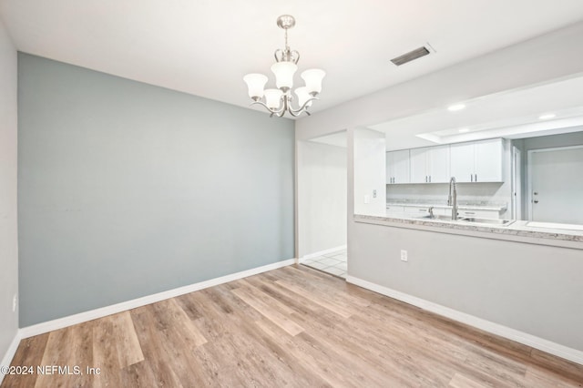 unfurnished dining area with sink, an inviting chandelier, and light wood-type flooring