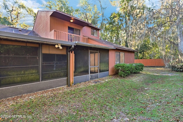 back of house featuring a balcony, a lawn, and a sunroom