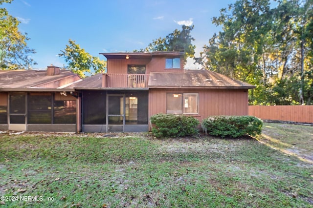 back of property featuring a yard, a sunroom, and a balcony