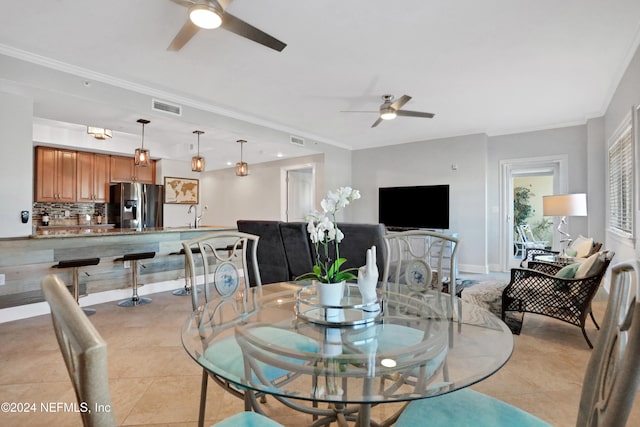 tiled dining room with ceiling fan, crown molding, and sink