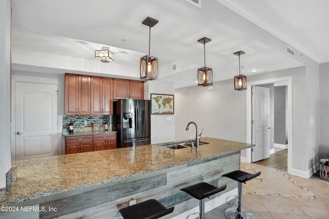 kitchen featuring kitchen peninsula, stainless steel fridge, light stone counters, sink, and decorative light fixtures