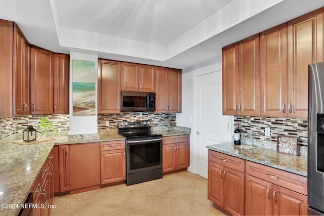 kitchen with stainless steel appliances, light stone counters, and a tray ceiling