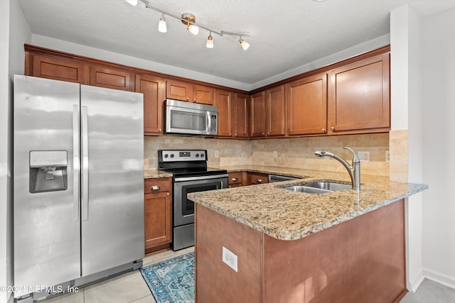 kitchen with light stone counters, kitchen peninsula, sink, and appliances with stainless steel finishes