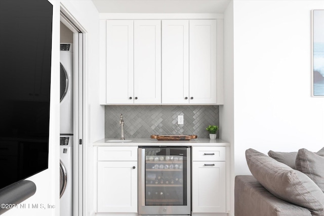 bar featuring backsplash, sink, wine cooler, white cabinetry, and stacked washer / dryer