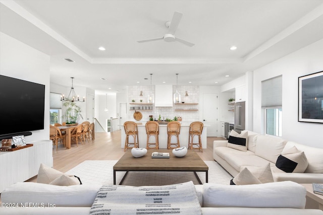 living room with a raised ceiling, light hardwood / wood-style flooring, and ceiling fan with notable chandelier