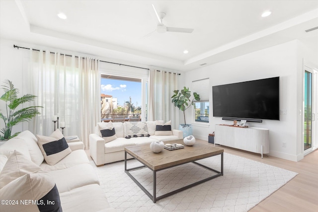 living room featuring a tray ceiling, ceiling fan, and light hardwood / wood-style floors