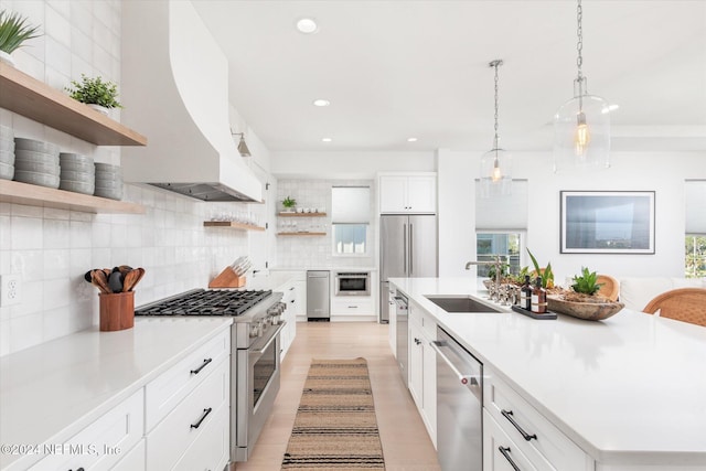 kitchen with custom exhaust hood, high end appliances, sink, pendant lighting, and white cabinetry