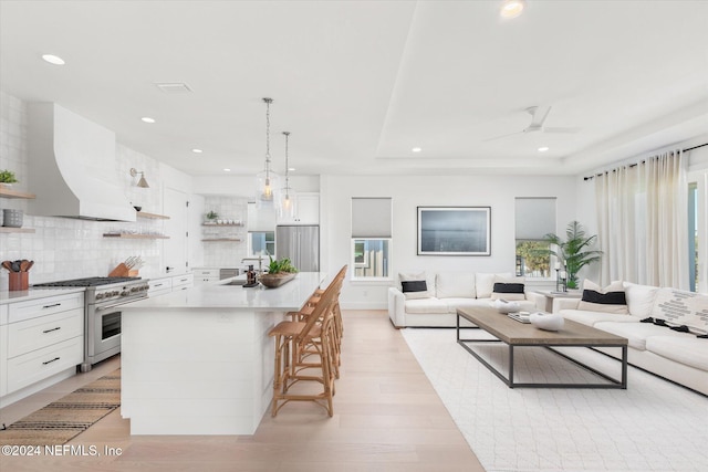 kitchen featuring wall chimney exhaust hood, high end stove, pendant lighting, a center island with sink, and white cabinets