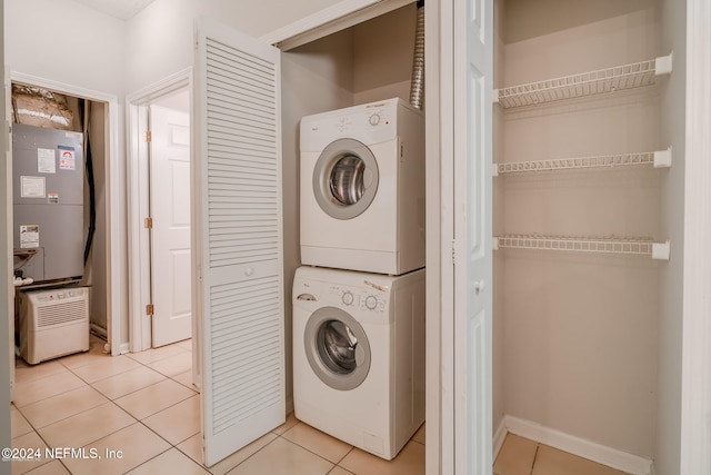 clothes washing area featuring light tile patterned flooring, stacked washer and dryer, and heating unit