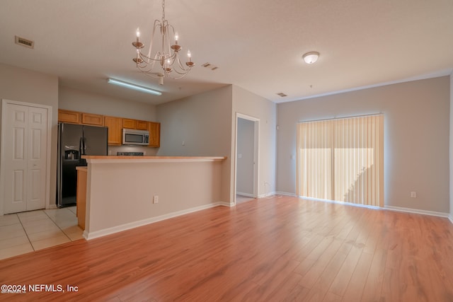 kitchen with light wood-type flooring, light brown cabinetry, decorative light fixtures, black fridge with ice dispenser, and a chandelier