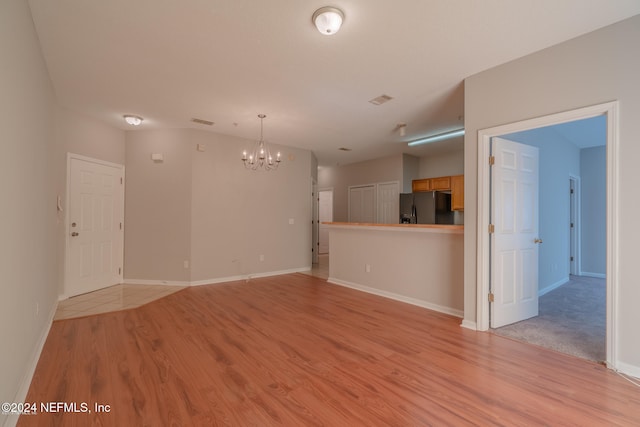 unfurnished living room with light wood-type flooring and a chandelier