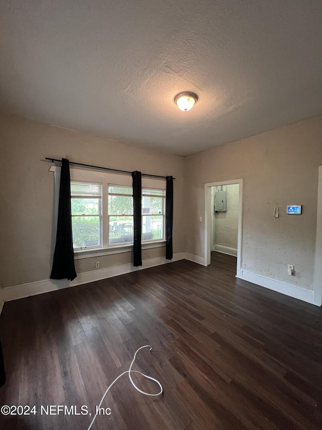 empty room featuring a textured ceiling, dark hardwood / wood-style flooring, and electric panel