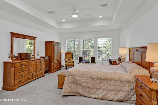 bedroom with ceiling fan, light colored carpet, and a tray ceiling