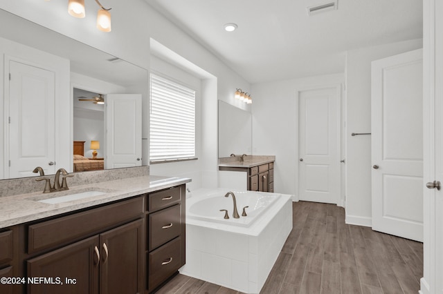 bathroom with tiled tub, ceiling fan, hardwood / wood-style floors, and vanity