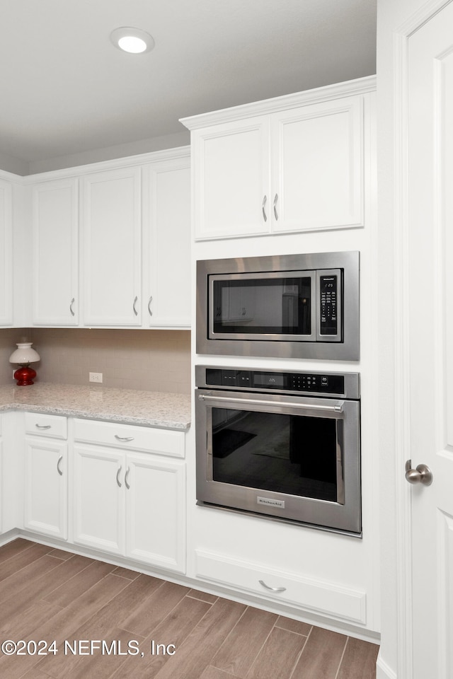 kitchen featuring light stone countertops, white cabinets, light wood-type flooring, and appliances with stainless steel finishes