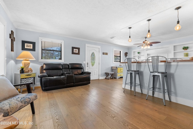 living room with ceiling fan, light hardwood / wood-style flooring, built in features, crown molding, and a textured ceiling