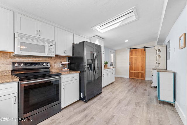 kitchen featuring white cabinets, light hardwood / wood-style flooring, vaulted ceiling with skylight, a barn door, and stainless steel appliances