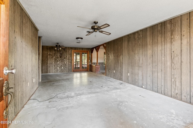 empty room with wood walls, ceiling fan, and a textured ceiling