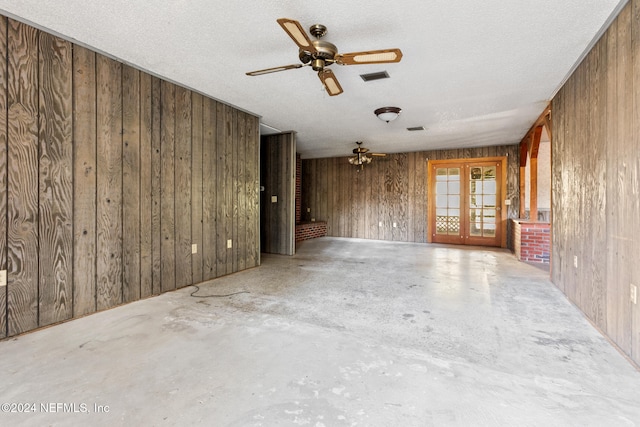 empty room featuring wood walls, french doors, concrete floors, and a textured ceiling