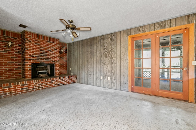 unfurnished living room with a textured ceiling, ceiling fan, and wooden walls