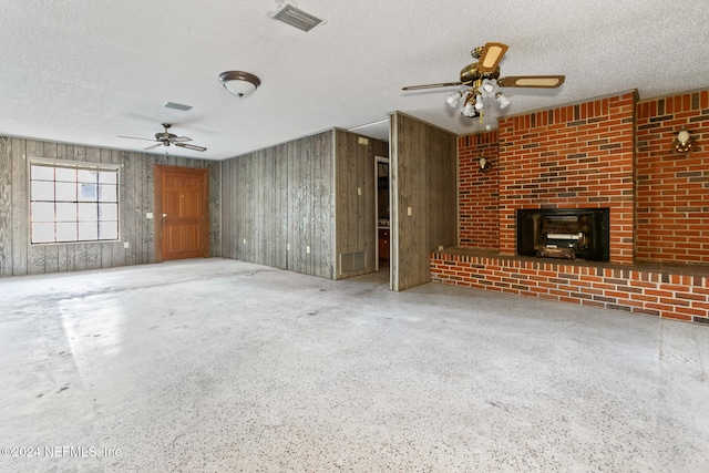 unfurnished living room featuring a textured ceiling, a brick fireplace, ceiling fan, and wood walls