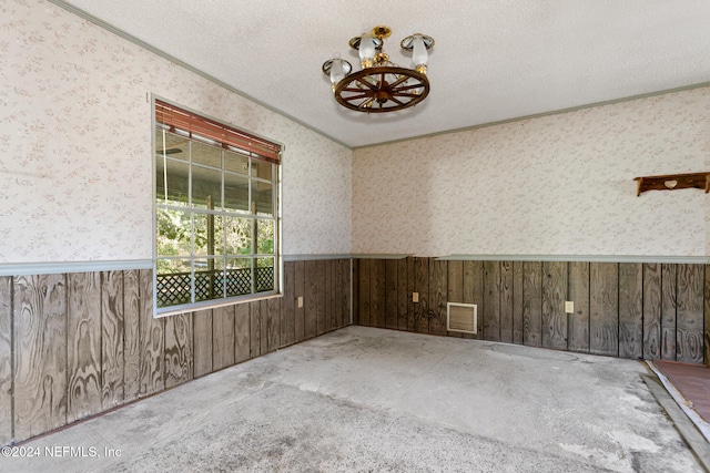 carpeted empty room featuring a textured ceiling, ornamental molding, and wood walls