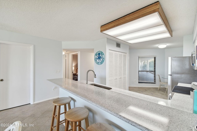 kitchen featuring sink, light stone countertops, a textured ceiling, a breakfast bar area, and stainless steel appliances