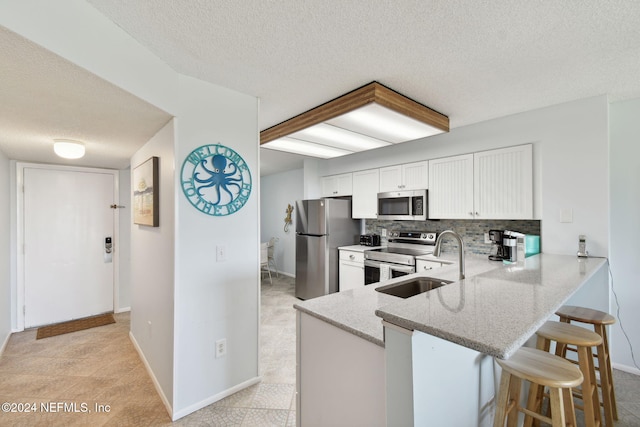 kitchen featuring sink, stainless steel appliances, kitchen peninsula, a kitchen bar, and white cabinets