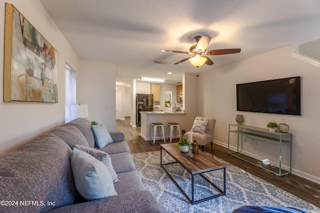 living room with a textured ceiling, ceiling fan, sink, and dark hardwood / wood-style floors